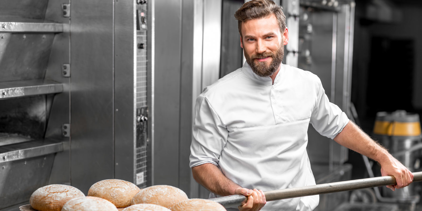 ein Bäcker beim Brot in den Ofen schieben in einer Bäckerei mit Menerga Lüftungssystem